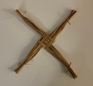 A Brigid’s cross with four equal arms woven in the center made of raffia.