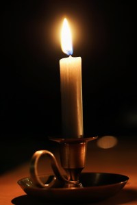 Lit white taper candle with holder which has a loop for ease of carrying.