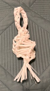 A corn dolly with a spiral form, a loop on top and a fringe on the bottom.